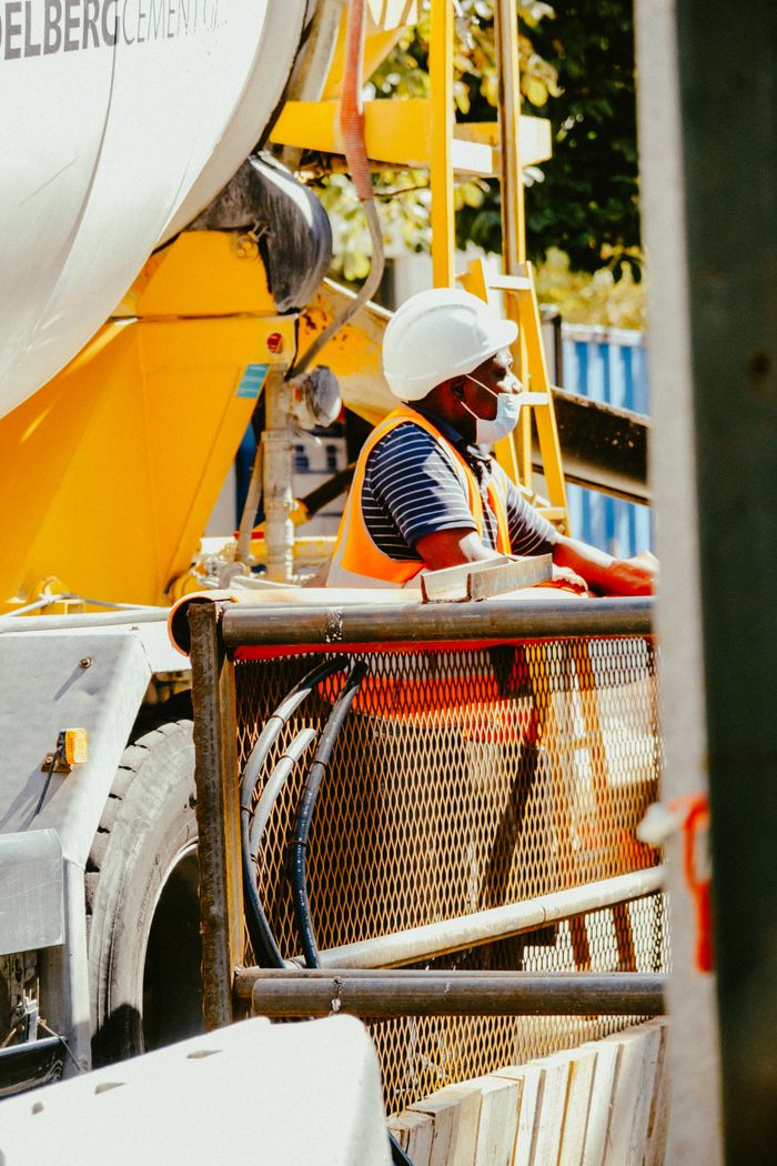 Construction worker in safety gear operating machinery at an industrial site during the day.